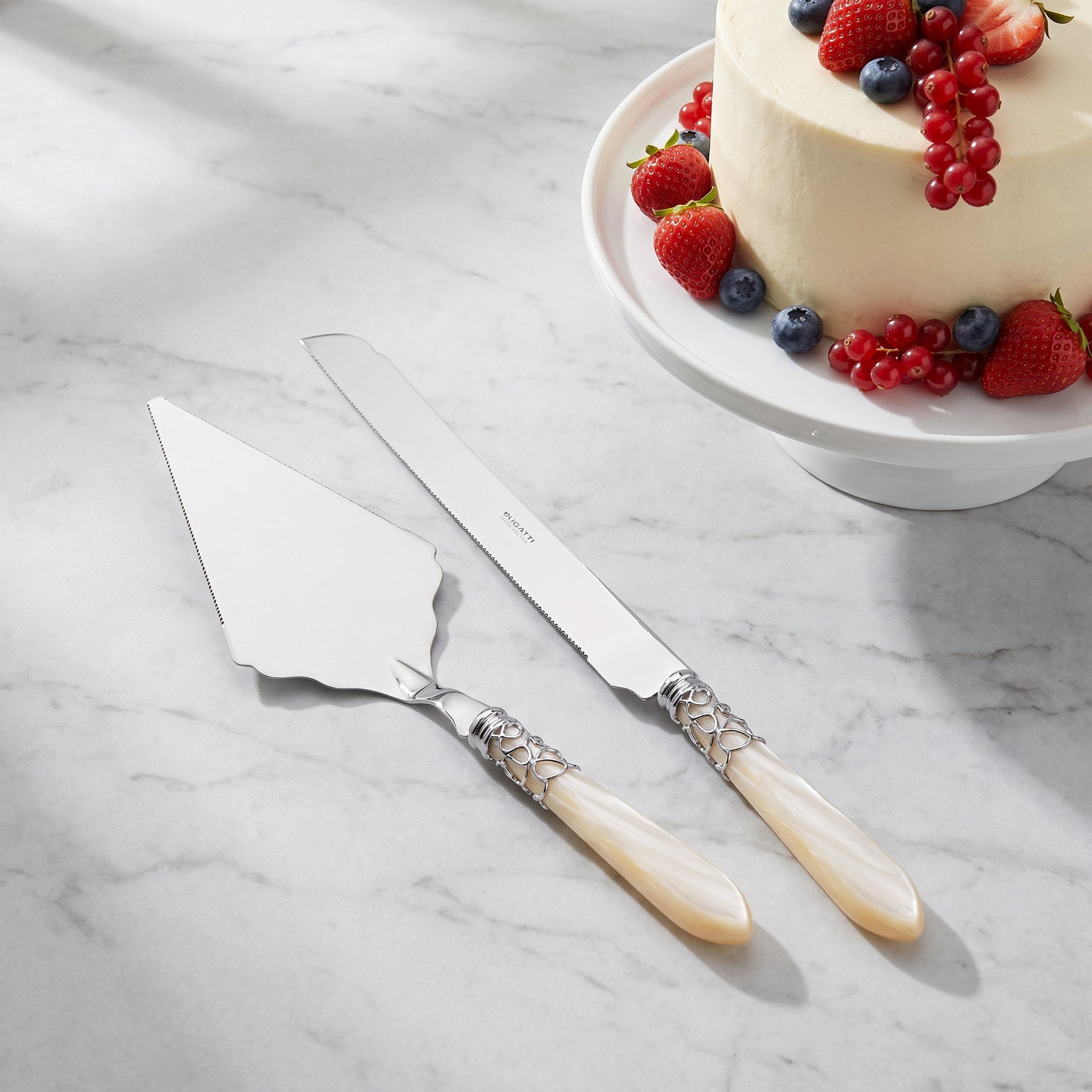 Large serrated cake serving set with a fruit-dressed celebration cake on grey marble